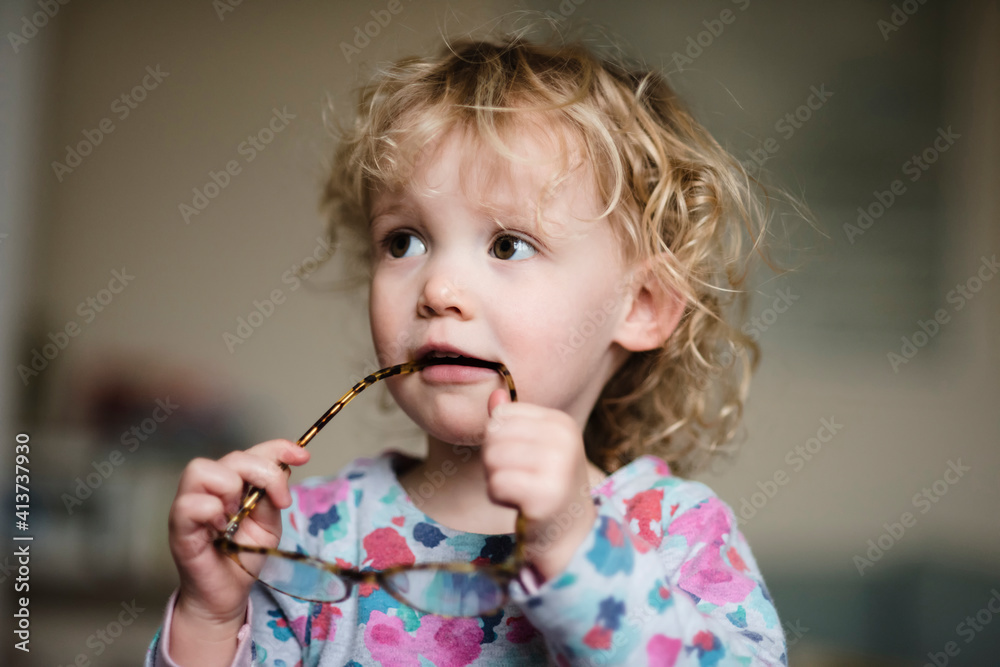 Close-up of girl with eyeglasses in mouth looking away while standing at home Close-up of girl with eyeglasses in mouth looking away while standing at home