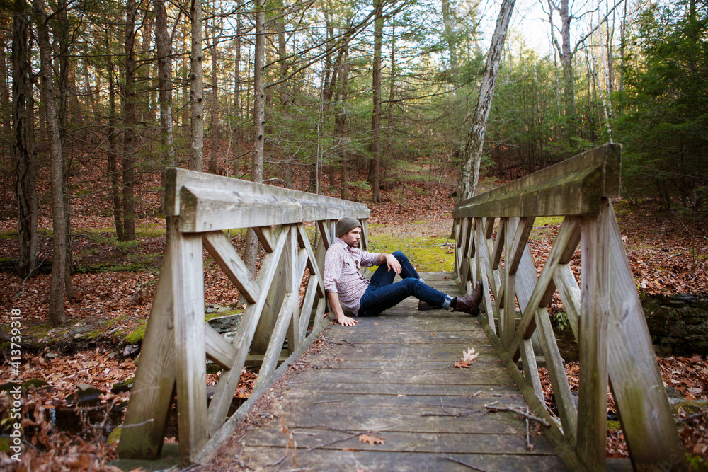 Side view of thoughtful man sitting on footbridge in forest Side view of thoughtful man sitting on footbridge in forest