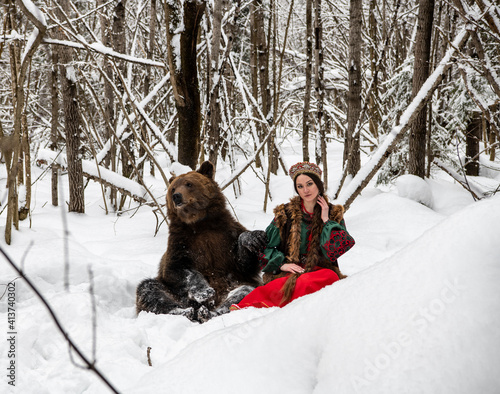 Russian beauty in folk national dress with a brown bear with a winter forest