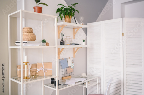 Background image empty home office working space in cozy apartment with modern scandinavian design. White table folding screen shelving stylish decor elements, stationery, houseplants in wicker pots.