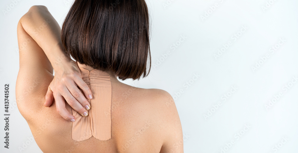 Kinesiology beige taping on the human back on a gray background with a copy space. Dynamic functional bandage taping on the girl's neck. Solution for back and neck pain. Headache. Kinesiology beige taping on the human back on a gray background with a copy space. Dynamic functional bandage taping on the girl's neck. Solution for back and neck pain. Headache.
