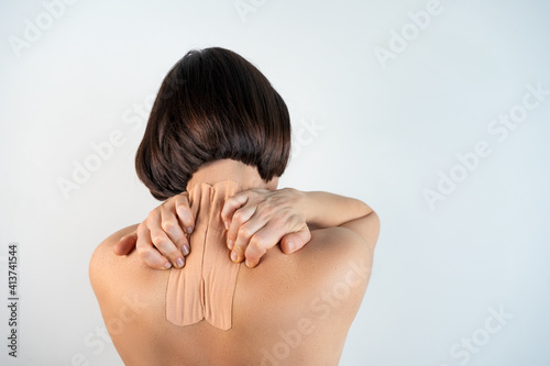 Kinesiology beige taping on the human back on a gray background with a copy space. Dynamic functional bandage taping on the girl's neck. Solution for back and neck pain. Headache.