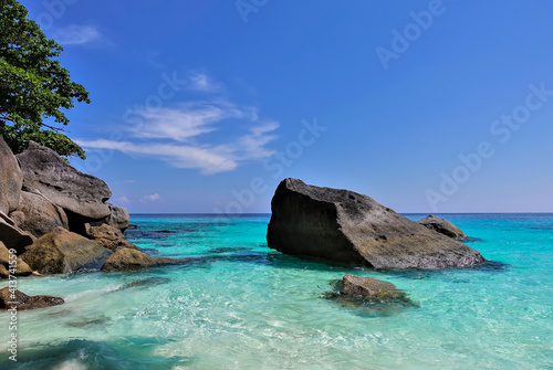 The aquamarine Andaman Sea is clear and calm. Huge picturesque boulders protrude from the water. White clouds in the azure sky. Thailand. Similan Islands.