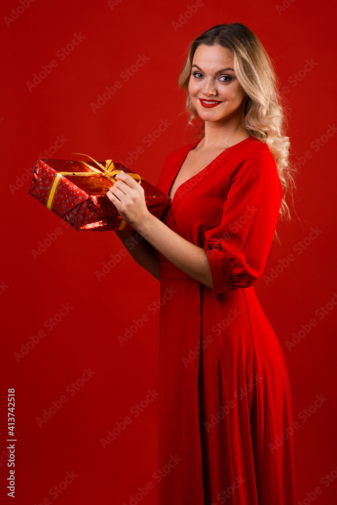 Give gifts for the holiday. Cheerful young woman in a red dress with a red gift box in her hands. Give gifts for the holiday. Cheerful young woman in a red dress with a red gift box in her hands.