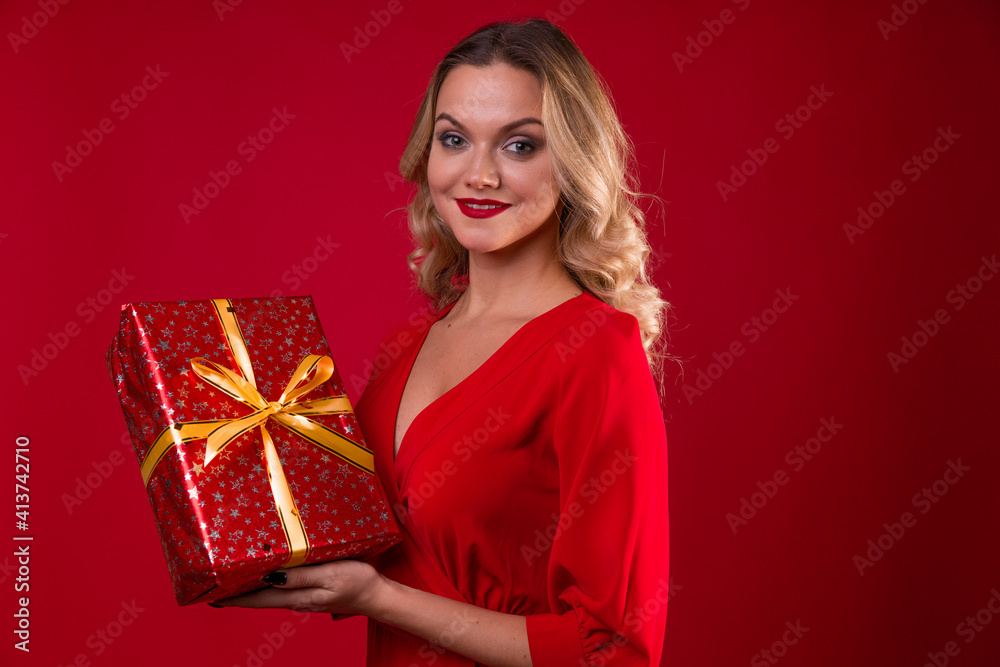 Give gifts for the holiday. Cheerful young woman in a red dress with a red gift box in her hands. Give gifts for the holiday. Cheerful young woman in a red dress with a red gift box in her hands.