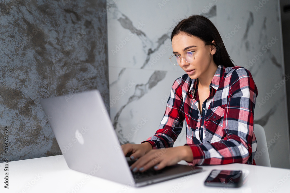 Pretty young woman working with laptop and documents in the kitchen at home. Pretty young woman working with laptop and documents in the kitchen at home.