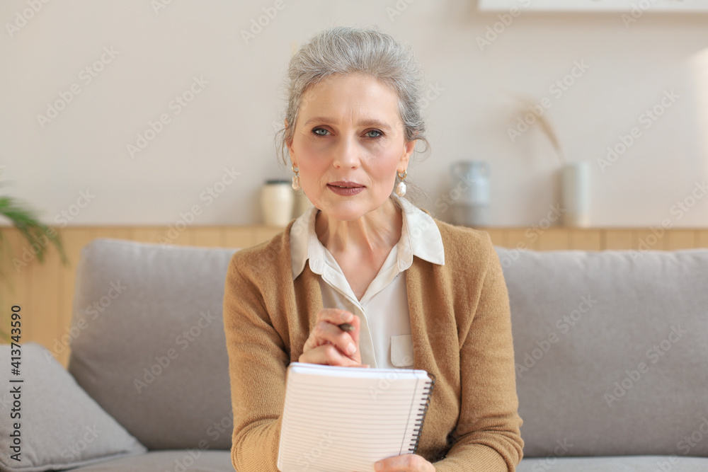 Attractive mature woman sitting on the couch and making notes in diary. Attractive mature woman sitting on the couch and making notes in diary.