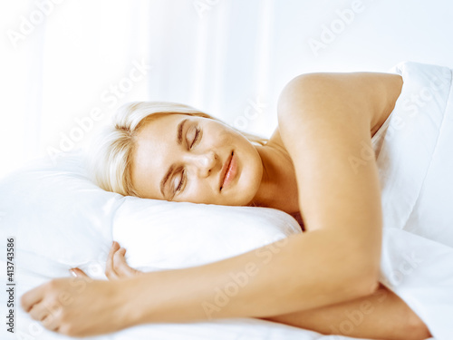 Beautiful young woman sleeping while lying in bed comfortably and blissfully. Good and sunny morning concept