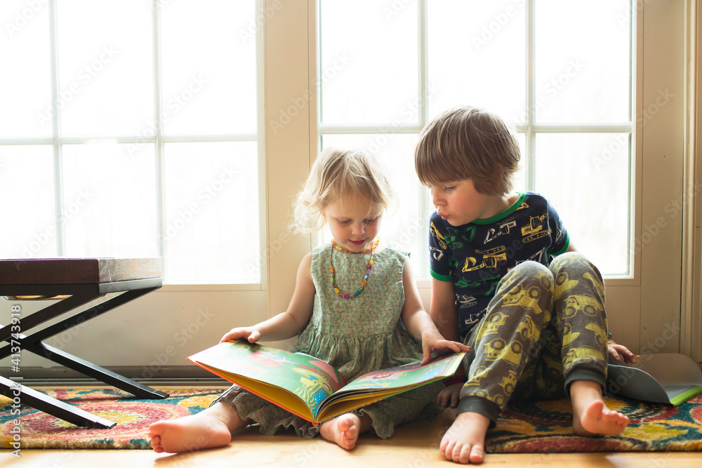 Siblings looking at picture book while sitting by window at home Siblings looking at picture book while sitting by window at home