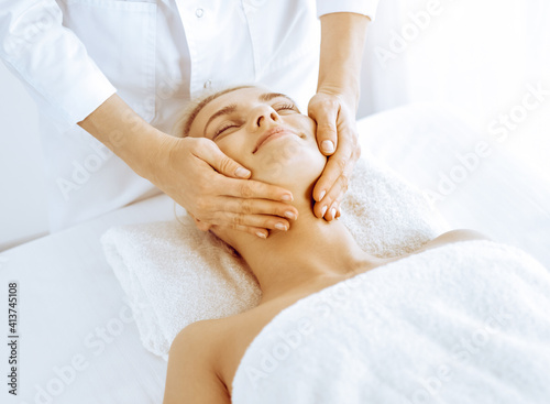 Beautiful blonde woman enjoying facial massage in spa center. Relaxing treatment in medicine and beauty concepts