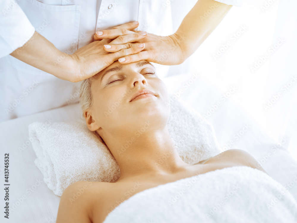 Beautiful blonde woman enjoying facial massage in spa center. Relaxing treatment in medicine and beauty concepts