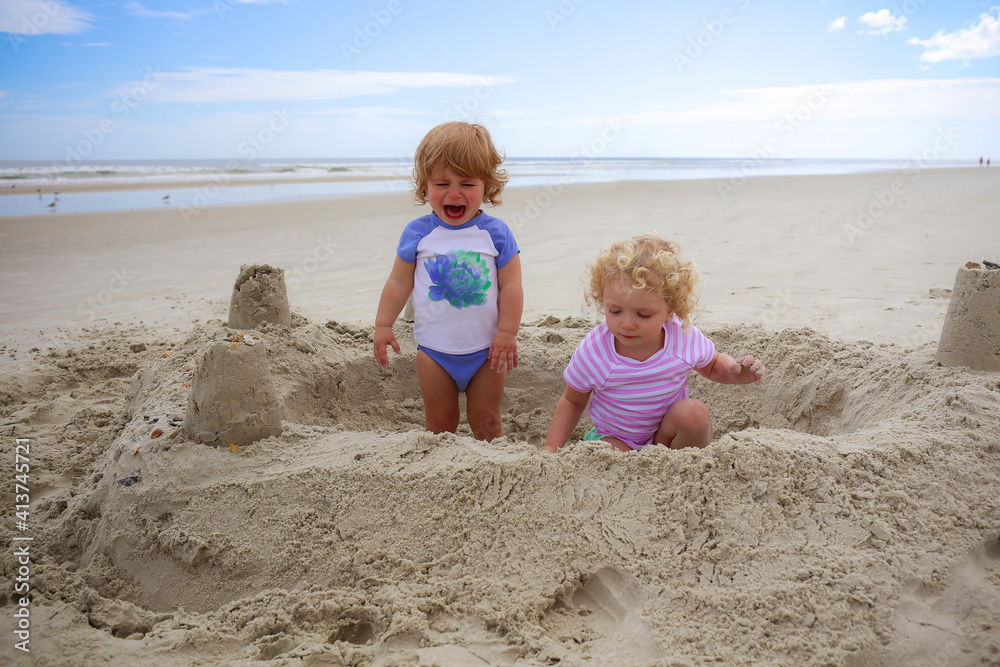 Boy crying while girl playing with sand at beach Boy crying while girl playing with sand at beach