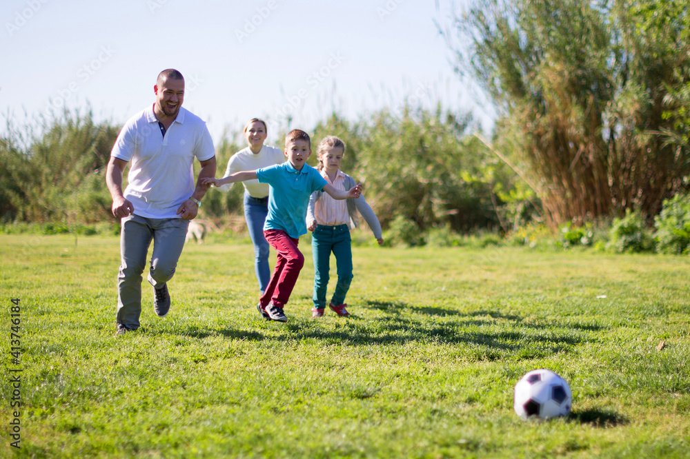 Obraz premium Father with mother with two children enjoy playing soccer on lawn in summer park