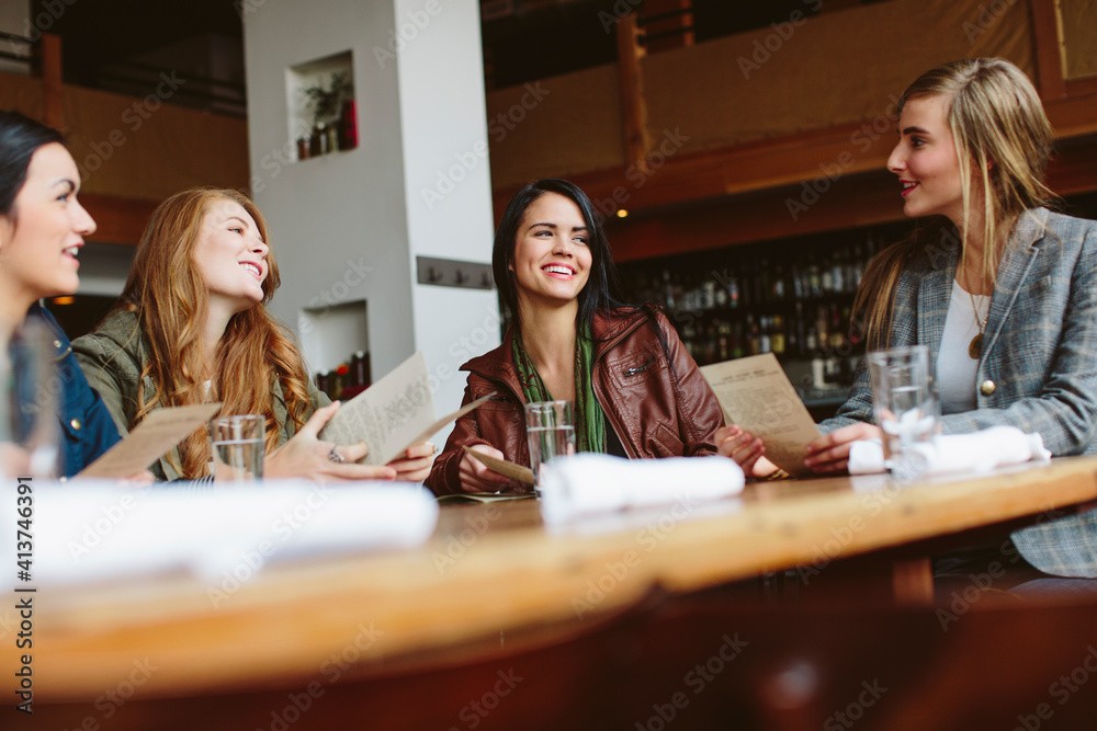 Happy female friends holding menu while talking at table in restaurant Happy female friends holding menu while talking at table in restaurant
