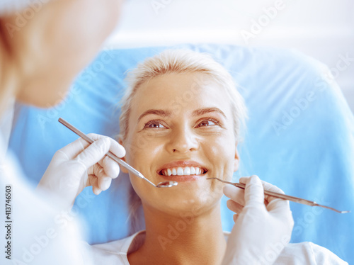 Smiling blonde woman examined by dentist at dental clinic. Healthy teeth in medicine concept