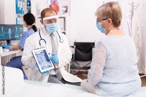 9Hospital specialist with face mask discussing digital x-ray holding tablet pc in the course of covid pandemic. Medical physician specialist during coronavirus outbreak discussing with patient.