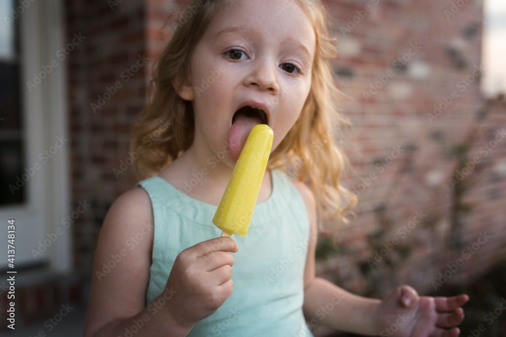 Portrait of girl eating popsicle stick while standing against house Portrait of girl eating popsicle stick while standing against house