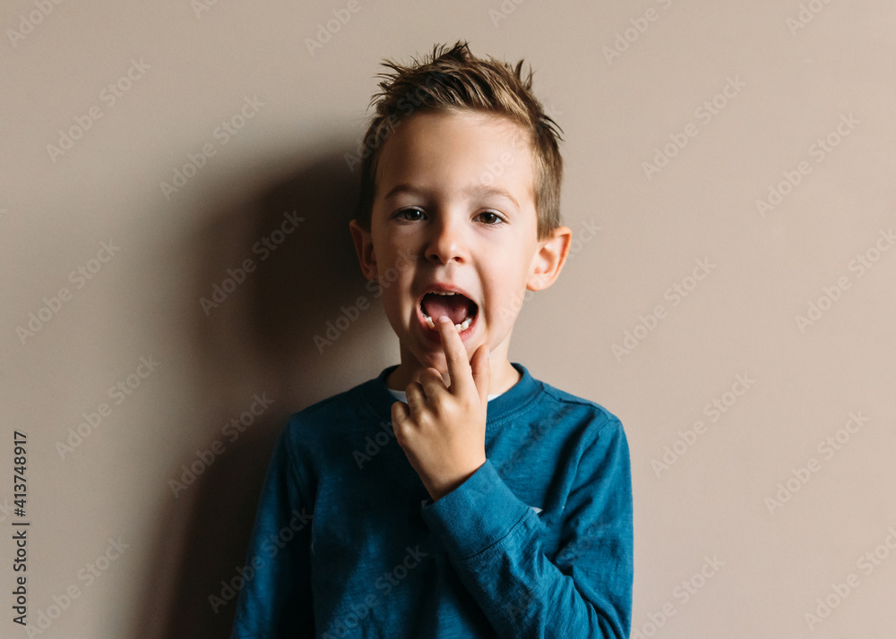 Portrait of boy touching teeth while standing against wall at home Portrait of boy touching teeth while standing against wall at home