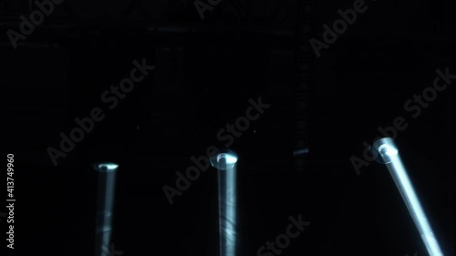 Dynamic white beams of stage light on black studio background. The searchlight spins, turns and emits light beams. Show of holograms. Lighting equipment and effects for holidays and parties. Close up. photo