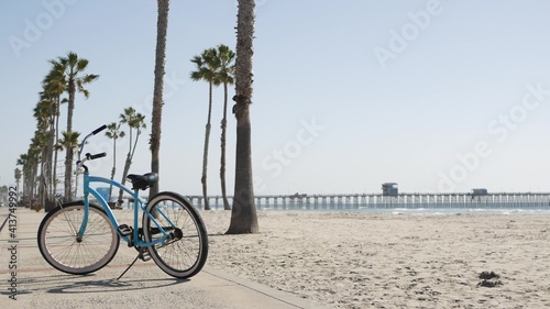 Blue bicycle, cruiser bike by sandy ocean beach, pacific coast near Oceanside pier, California USA. Summertime vacations, sea shore. Vintage cycle, tropical palm trees, lifeguard tower watchtower hut