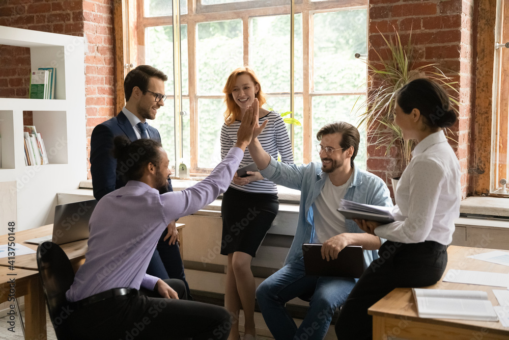 Overjoyed multiethnic male employees give high five motivated shared work success or promotion at meeting. Smiling multiracial men colleagues celebrate good job results engaged in office briefing.