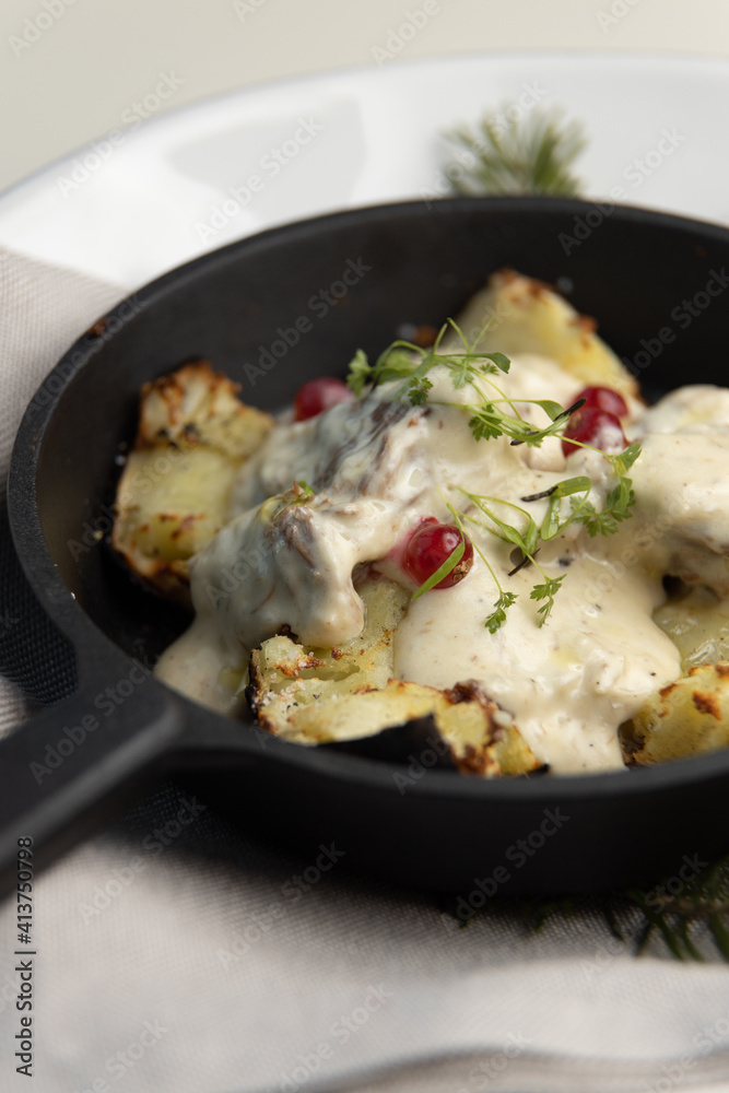 Fried potatoes in a frying pan with cream gravy and berries close-up. Potatoes baked in coals with herbs, restaurant serving of the dish. Fried potatoes in a frying pan with cream gravy and berries close-up. Potatoes baked in coals with herbs, restaurant serving of the dish.
