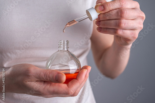 Woman is holding a bottle of aromatic oil and a drop is falling from the pipette. Concept of natural care cosmetics and skin and hair care. Closeup