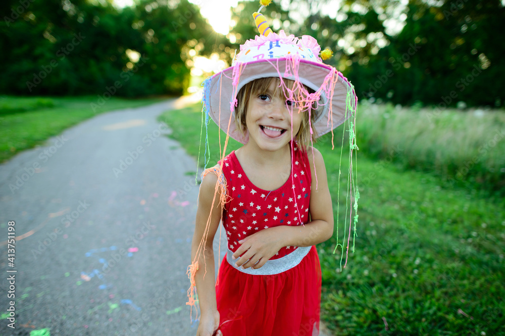 Girl in birthday cake hat looking away while sticking out tongue on road Girl in birthday cake hat looking away while sticking out tongue on road