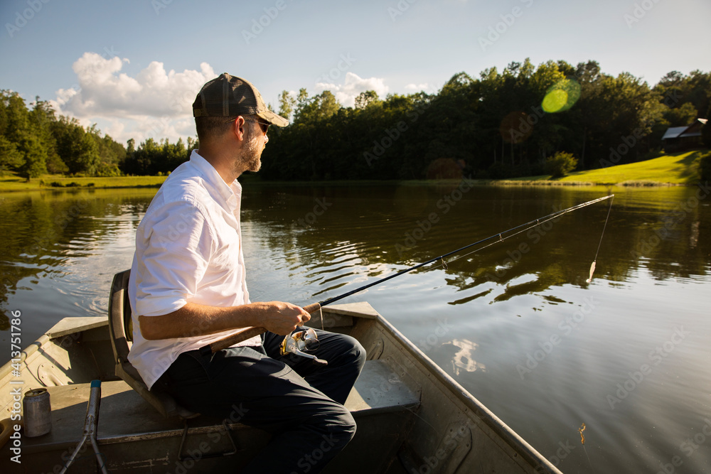 Man fishing while sitting in rowboat on lake Man fishing while sitting in rowboat on lake