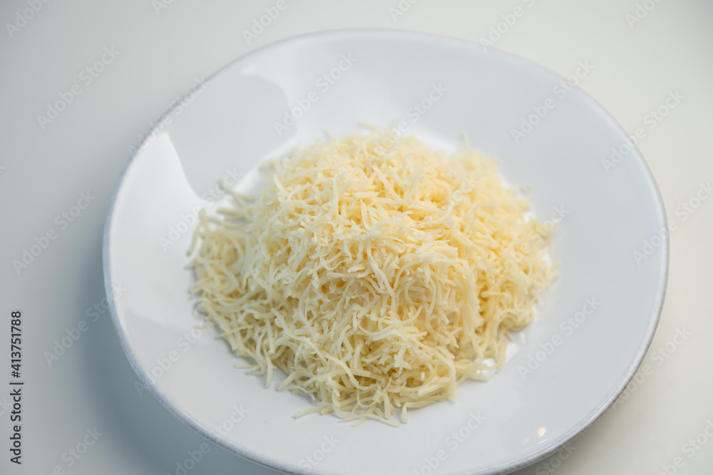 Grated cheese on a white plate close-up. Grated cheese salad, restaurant serving of the dish. Grated cheese on a white plate close-up. Grated cheese salad, restaurant serving of the dish.