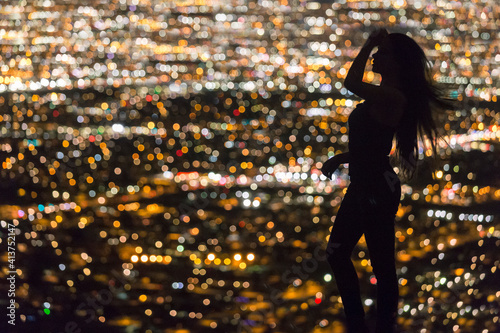 Silhouette woman with hand in hair standing against illuminated cityscape at South Mountain Park photo