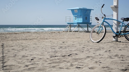 Blue bicycle, cruiser bike by ocean beach, pacific coast, Oceanside California USA. Summertime vacations, sea shore. Vintage cycle on sand near lifeguard tower or watchtower hut. Sky and water waves.