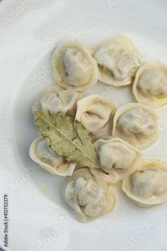 Meat dumplings on a white plate with bay leaf. Restaurant serving dishes, close-up.