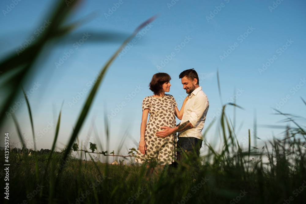 Low angle view of man touching PRegnant woman's stomach while standing on grassy field against clear sky Low angle view of man touching PRegnant woman's stomach while standing on grassy field against clear sky