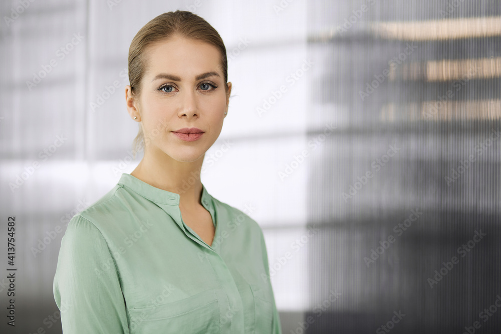 Beautiful adult business woman dressed in green blouse standing straight in office. Business headshot or portrait Beautiful adult business woman dressed in green blouse standing straight in office. Business headshot or portrait
