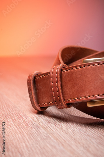 Leather brown belt twisted in a sign of infinity on a wooden orange background. High quality photo © ISliM