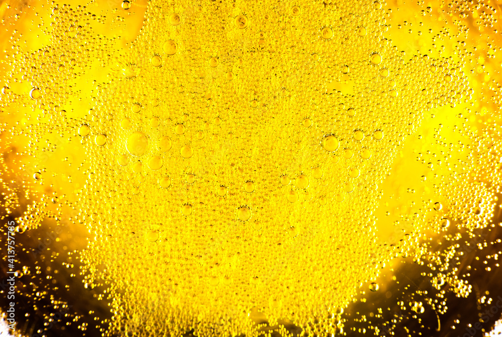 Liquid gold-yellow gasoline bubbles background on beer or champagne glass. Close up, macro shot.