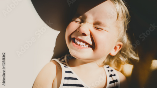 Cutest little girl smiling and squinting in sunlight. Happy toddler having fun. Portrait of playful child preschool age. Lifestyle photography.