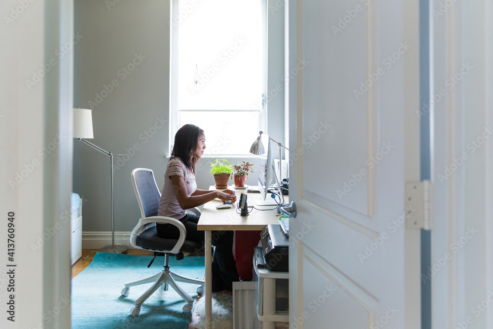 Woman working on desktop computer at home office seen through doorway Woman working on desktop computer at home office seen through doorway