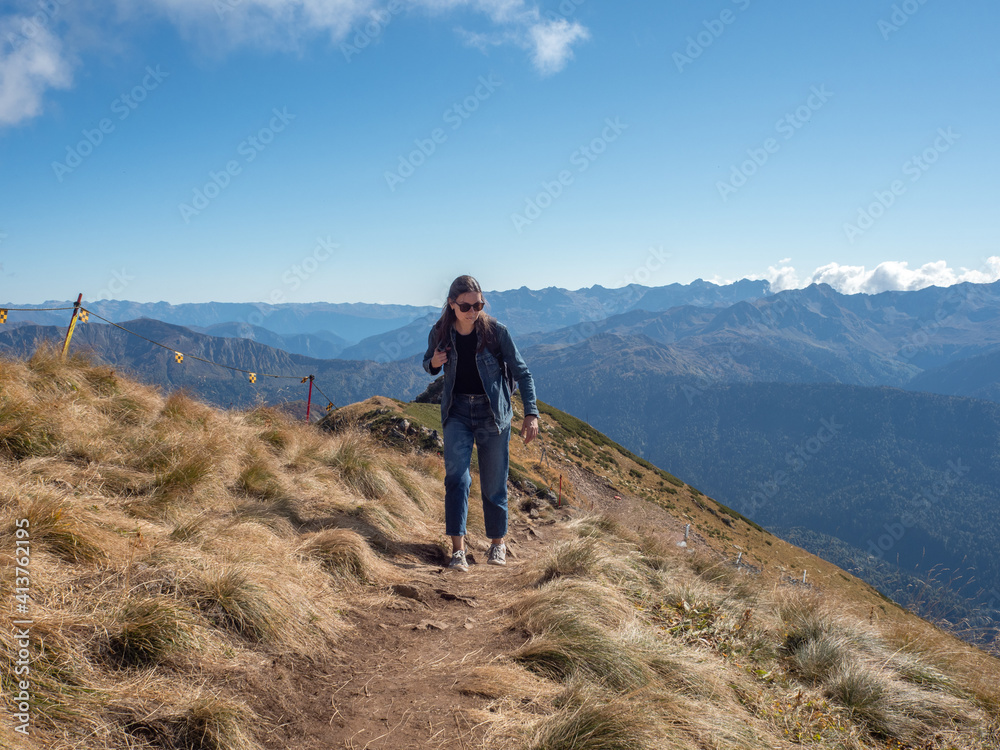 Hiking in the mountains, a young female tourist with a backpack is walking along