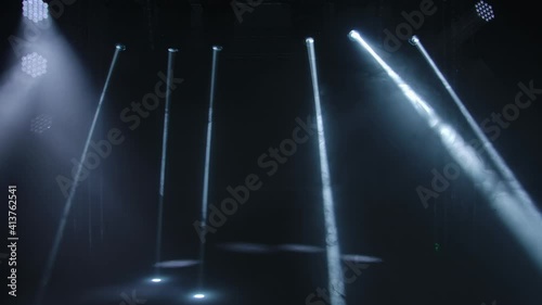 Dynamic white beams of stage light on black studio background. The searchlight spins, turns and emits light beams. Show of holograms. Lighting equipment and effects for holidays and parties. photo