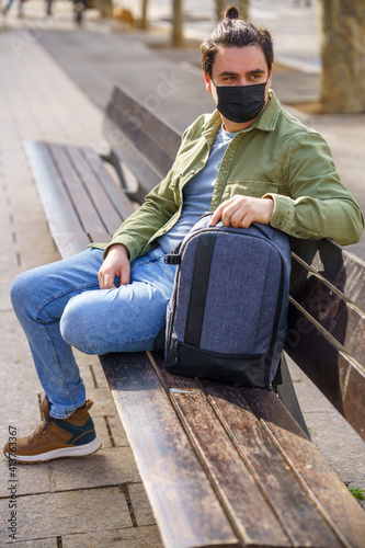 Man sitting on a bench with one hand leaning on his backpack