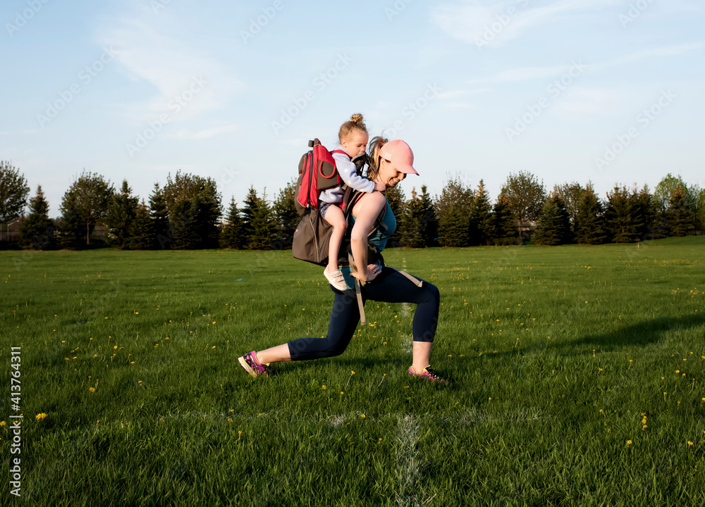Side view of mother carrying daughter while exercising on grassy field against sky at park Side view of mother carrying daughter while exercising on grassy field against sky at park