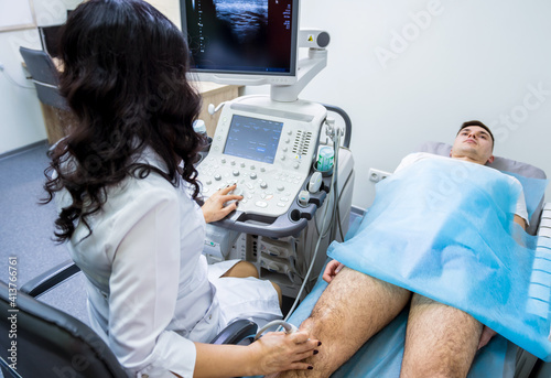 Doctor using ultrasound scanning machine examining injured knee