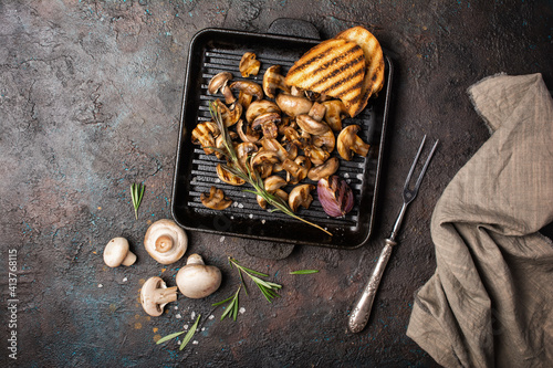 Spicy fried mushrooms on grill pan with onion, rosemary and bread