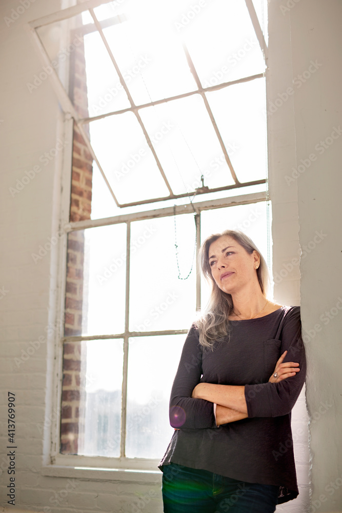 Thoughtful woman with arms crossed leaning on wall at home Thoughtful woman with arms crossed leaning on wall at home