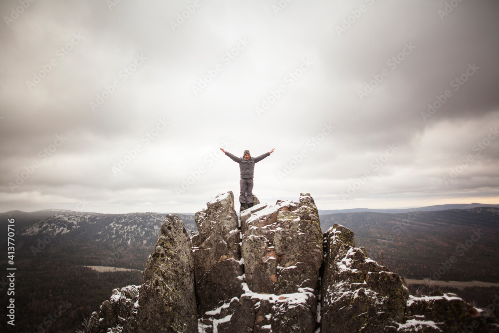 Man with arms outstretched standing on mountain against cloudy sky