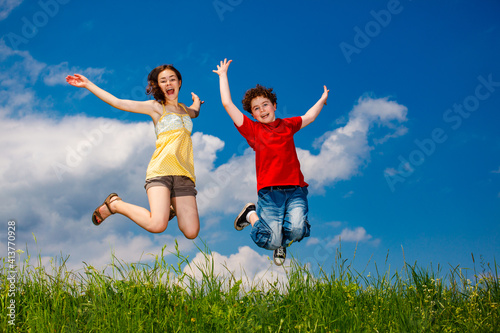 Girl and boy running, jumping against blue sky 