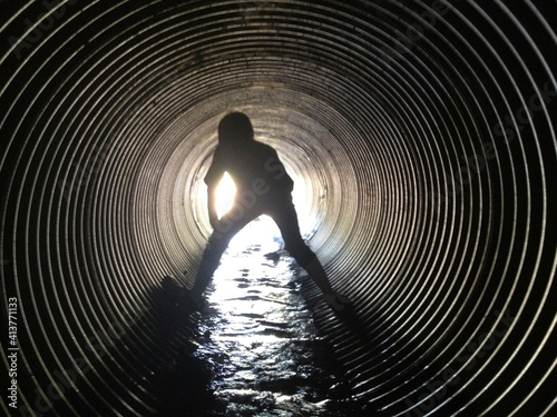 Rear view of silhouette boy standing in sewage tunnel