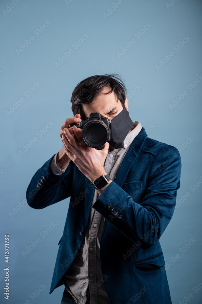 Obraz premium Portrait of positive photographer, man with medical mask holding professional digital dslr camera